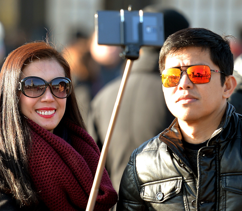 Tourists use a “selfie stick” in London. A French palace and a British museum have joined the growing list of tourist attractions banning the devices. The Associated Press