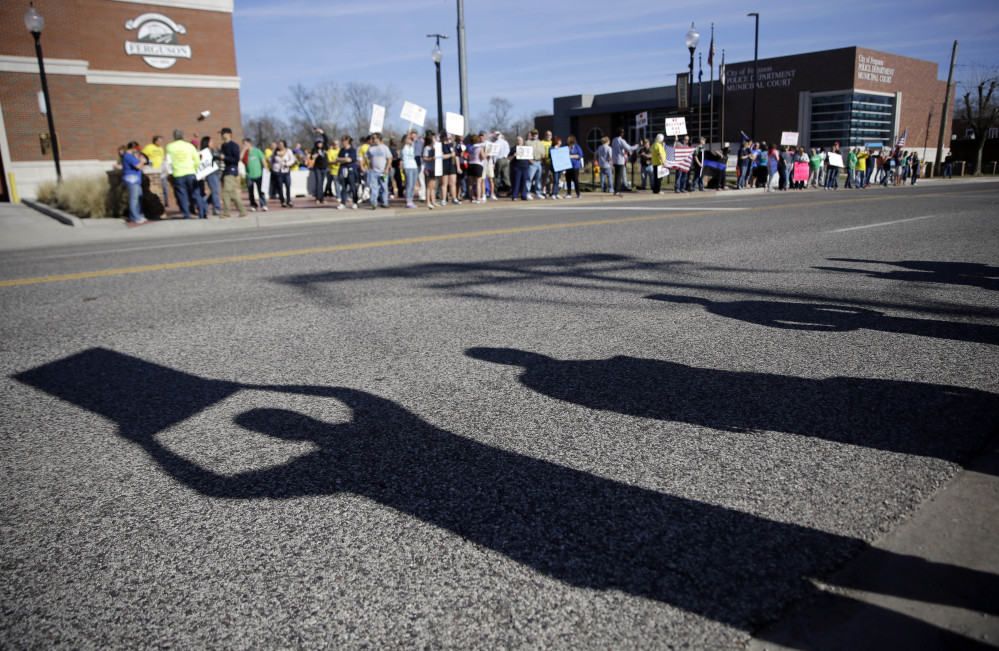 About 100 pro-police demonstrators hold signs outside the Ferguson Police Department as the shadows of counter demonstrators are seen on the street Sunday in Ferguson, Mo.