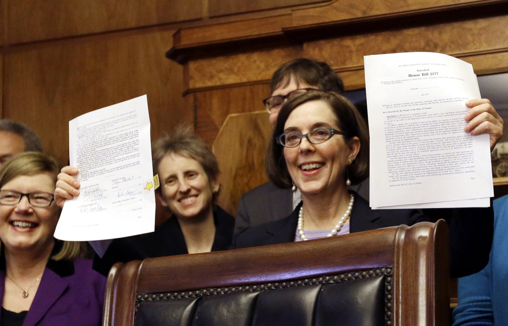 Oregon Gov. Kate Brown holds up an automatic voter registration bill after signing it Monday. Seventeen years after Oregon decided to become the first state in the nation to hold all elections by mail, it is taking another step to encourage more people to vote.
