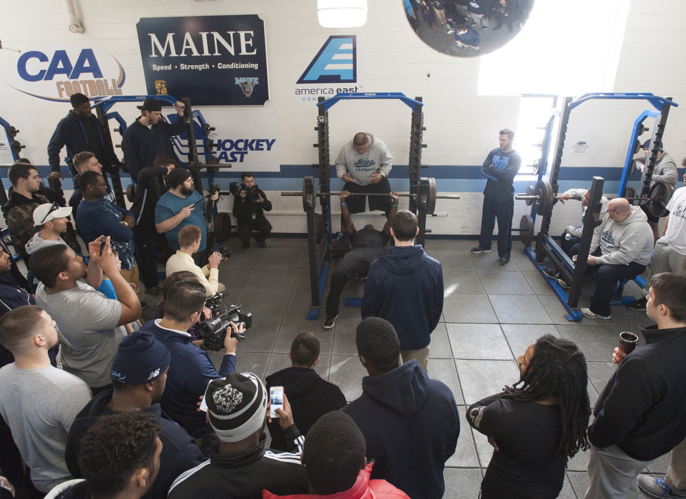 Teammates and media gather around UMaine defensive back Axel Ofori Jr. as he bench presses for Brandon Yeargan, a scout from the New England Patriots, at the UMaine weight room during Pro Day on Thursday in Orono.