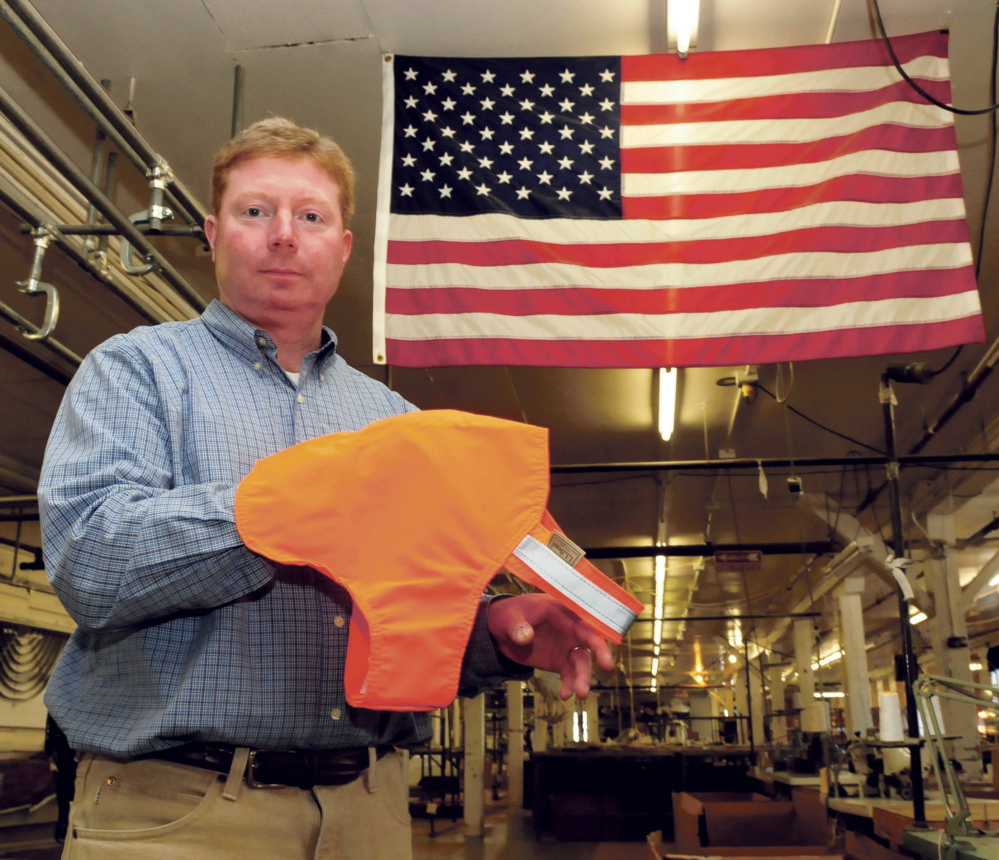 Bill Swain, owner of Maine Stitching Specialties in Skowhegan, holds an L.L. Bean No Fly Zone dog vest near an American flag made at the Skowhegan company.