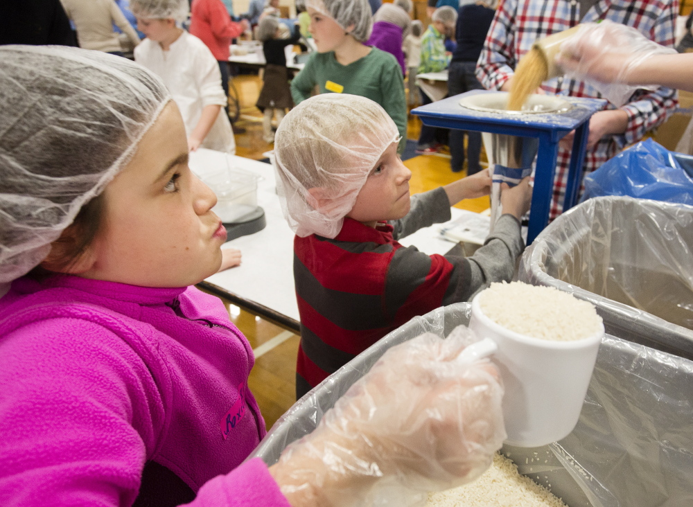 Volunteer Roxie Van Oosterun, 9, of Portland, left, awaits her turn to pour rice into a meal pack while Elias Bennett, 8, of Gray, holds a bag for filling beneath a funnel. The effort at Deering High School was organized by Million Meals Maine, a nonprofit started last year.