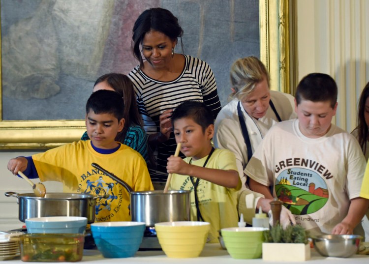 First lady Michelle Obama watches as school children prepare lunch in the East Room of the White House following the annual fall harvest of the White House Kitchen Garden in October 2014. The first lady is challenging the nation's children to dream up healthy lunch recipes, a now annual component of her Let's Move! campaign to reduce childhood obesity through diet and exercise.