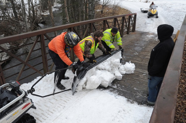 Parks and Recreation maintenance workers empty a sled load of snow from Goose Lake onto a snowless bridge in Anchorage, Alaska.  Crews have been moving snow into tunnels, covering bridges and bare spots in the trail in preparation for the ceremonial start of the Iditarod Trail Sled Dog Race.