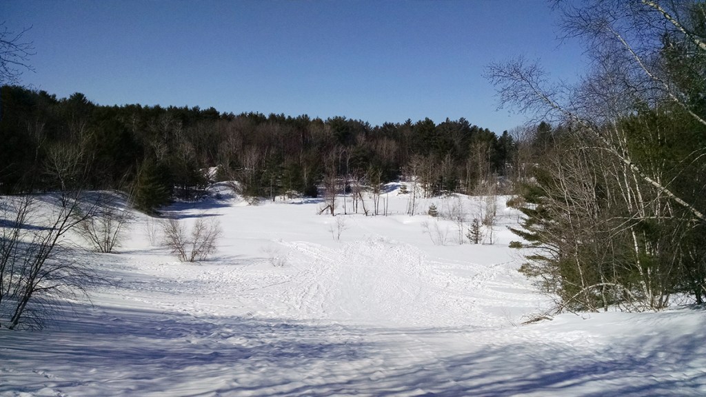 The development proposal would leave an old sand pit as a permanent open space  or a town park. This is a view from the top of the sand pit – which is a popular wintertime sledding hill – back toward the proposed roadway. Photo courtesy of Matt Teare