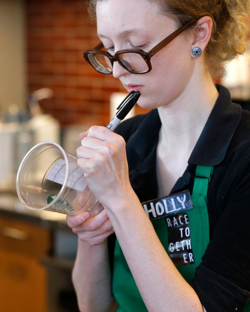 Holly Ainslie, a barista at a Starbucks store in Seattle, writes on a cup for an iced drink as she wears a "Race Together" sticker. Starbucks baristas will no longer write "Race Together" on customers' cups, ending a component of the company's diversity and racial inequality campaign, according to a memo.The Associated Press
