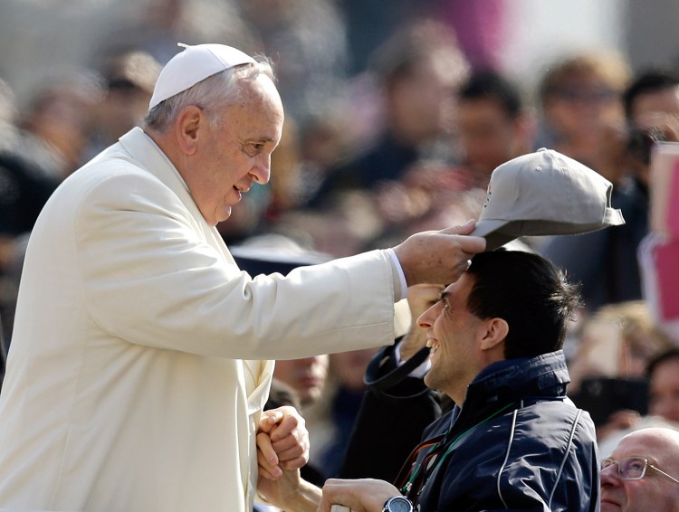 Pope Francis puts a cap on the head of a man as he arrives for his weekly general audience in St. Peter's Square at the Vatican on Wednesday.