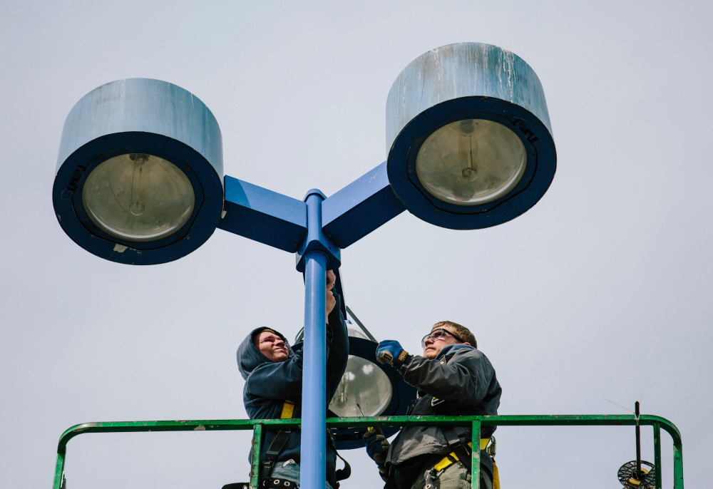 Seabee Electric employees Madison Hanson, left, and Nick Dyro install LED lights in The Maine Mall parking lot in South Portland on Wednesday. The LED lights will use one-third to one-half less power than the old lights.