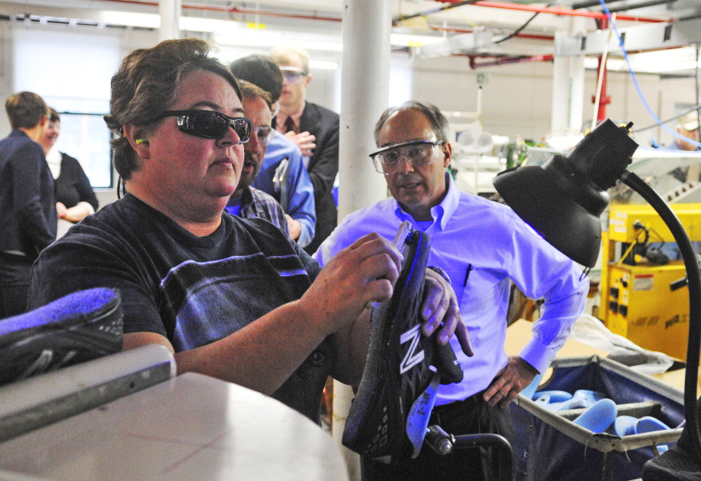 Working under ultraviolet lights, Tammie Ward spreads glue on a shoe as U.S. Rep. Bruce Poliquin, R-2nd District, watches during a tour of the New Balance factory on Friday in Norridgewock.