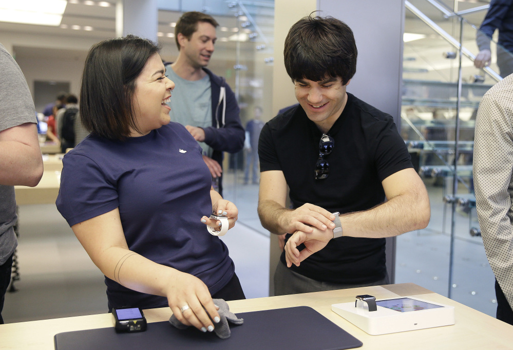 An Apple Store employee, left, laughs along with a customer Friday as he tries on the Cupertino, Calif.-based company’s latest innovation – the Apple Watch – in San Francisco. In the product’s debut, the only way to get one was online or through the Apple Store app. Shipments are scheduled to start April 24.