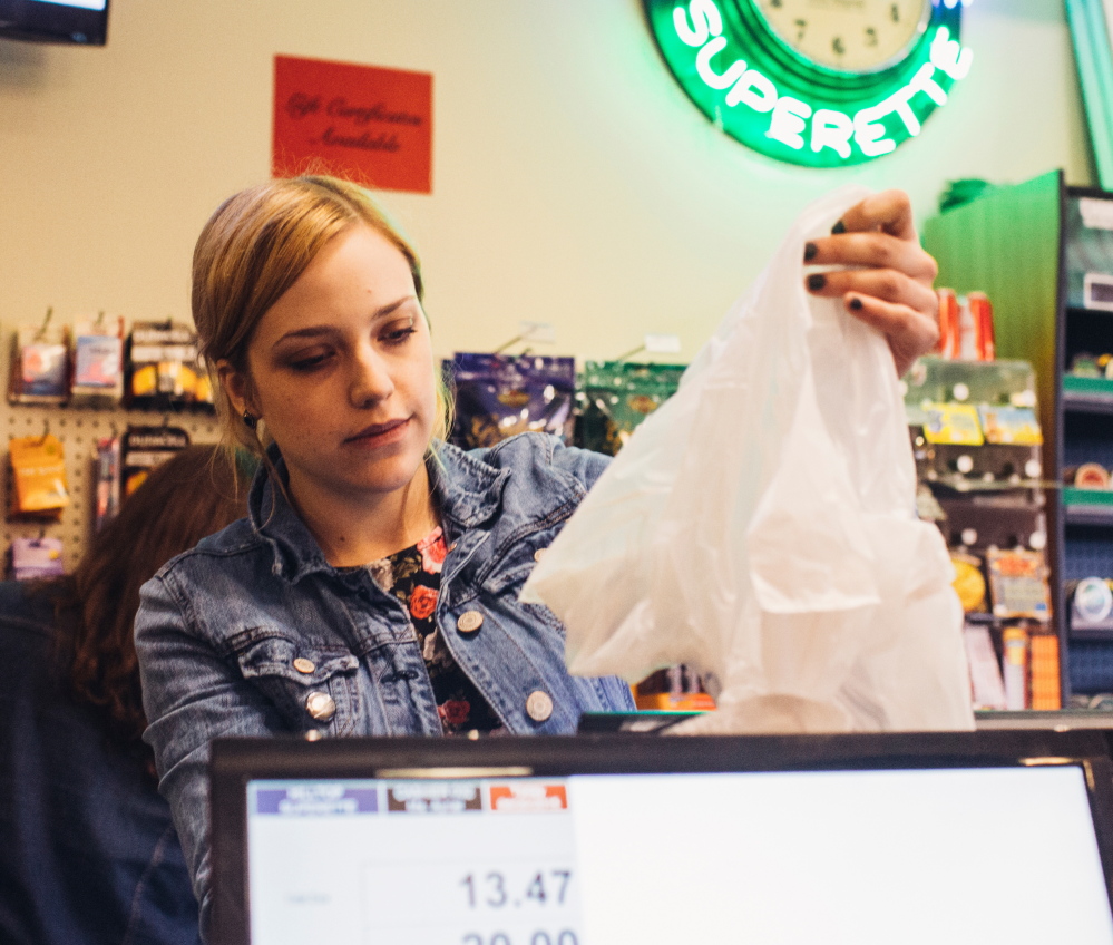 Hilltop Superette cashier Ayriel Chase prepares a plastic bag for a customer. Some shoppers carry items out in their hands to avoid a fee.