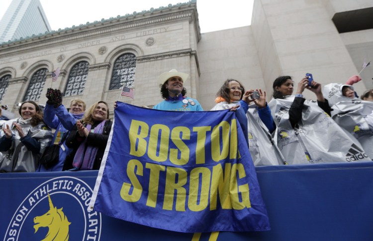 Carlos Arredondo, a 2013 Boston Marathon first-responder, holds a “Boston Strong” banner beside his wife, Melida, right, in the grandstand near the Boston Marathon finish line.