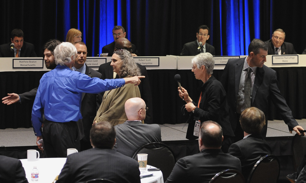 David Ludlow of Boston’s Jamaica Plain neighborhood, in blue on left, stands up to protest before he is escorted out by security as Connecticut Gov. Dannel P. Malloy and Maine Gov. Paul LePage, top right, listen during a panel meeting, Thursday, April 23, 2015, in Hartford, Conn. Ludlow accused the governors of indifference to climate change in an energy policy that increasingly relies on natural gas and efforts to build more fossil fuel pipelines.