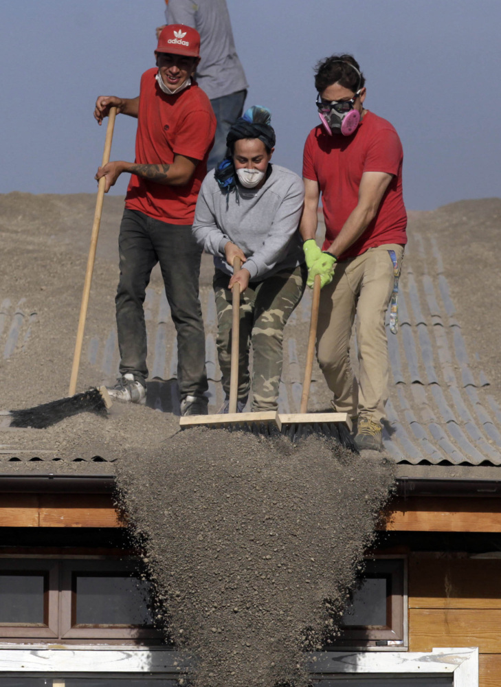 People sweep volcanic ash from a home’s roof in Puerto Varas, Chile, on Friday.