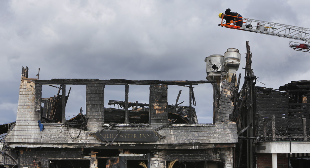 Perched on a ladder of an Ogunquit Fire Department truck, an investigator with the state Fire Marshal’s Office takes a photo of the Blue Water Inn in Ogunquit on Wedensday, the day after a windswept fire destroyed the building.