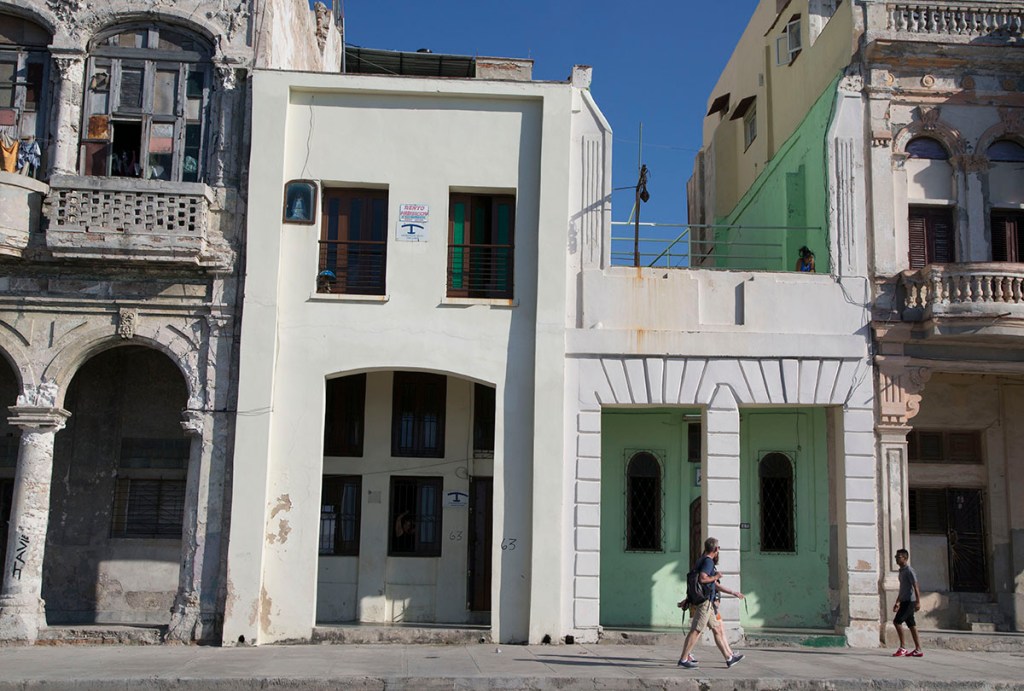 Tourists walk past two privately owned houses with rooms for rent in Havana. The Associated Press