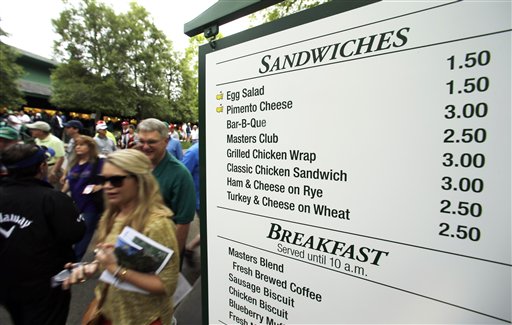 In this file photo taken Monday, April 6, 2015, patrons walk past a vendor sign during a practice round for the Masters golf tournament, in Augusta, Ga. At a time when buying a hot dog and a beer at any big event can mean a pricey tab and a credit card, Augusta National makes it easy to fill up in possibly the best value meal deal in all of sports with a menu that is pure South. The Associated Press