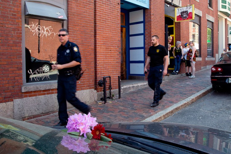 Portland police officers walk past flowers placed on the car that Treyjon Arsenault was driving on the night in 2015 when he was killed in a shooting at 26 Market St. in the Old Port.