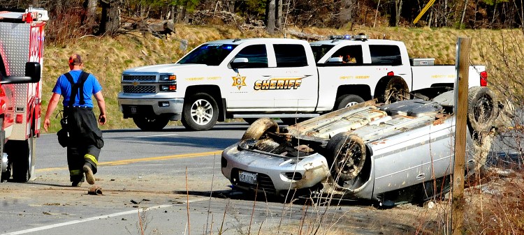 A firefighter walks past the overturned vehicle where, according to police at the scene, the single occupant died after the car rolled at the intersection of Route 201A and the Ward Hill Road in Norridgewock on Sunday. David Leaming/Morning Sentinel Staff Photographer