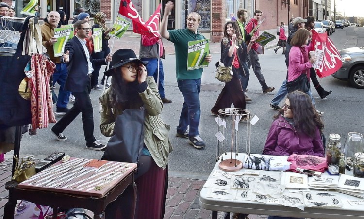 A group that supports raising the minimum wage to $15 an hour marches down Congress Street as artists Alice Shin, left, and Sara Inacio display their wares on Friday. Portland’s monthly art walk has a growing focus on political issues.