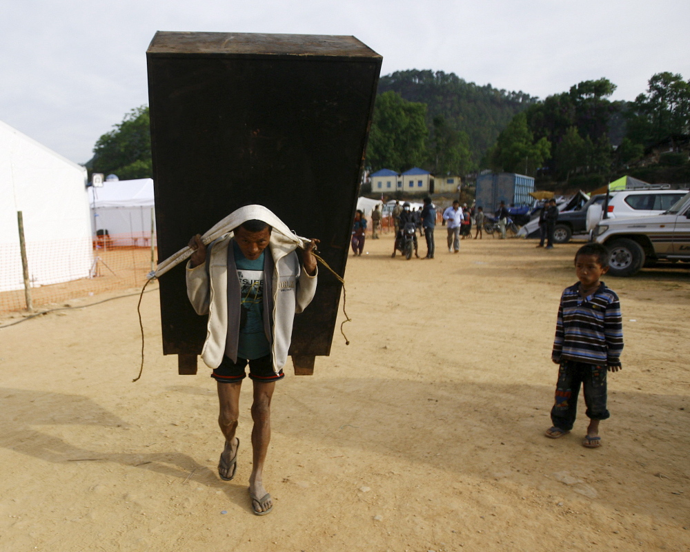 MAY 5: A man carries a cupboard after salvaging it from a collapsed house in Nepal on Tuesday. A woman from Maine is still missing more than a week after the earthquake.