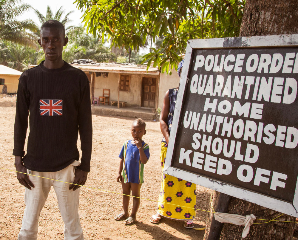 A man in Kambia, Sierra Leone, outside his home next to a board stating that his home is under quarantine due to the Ebola virus.