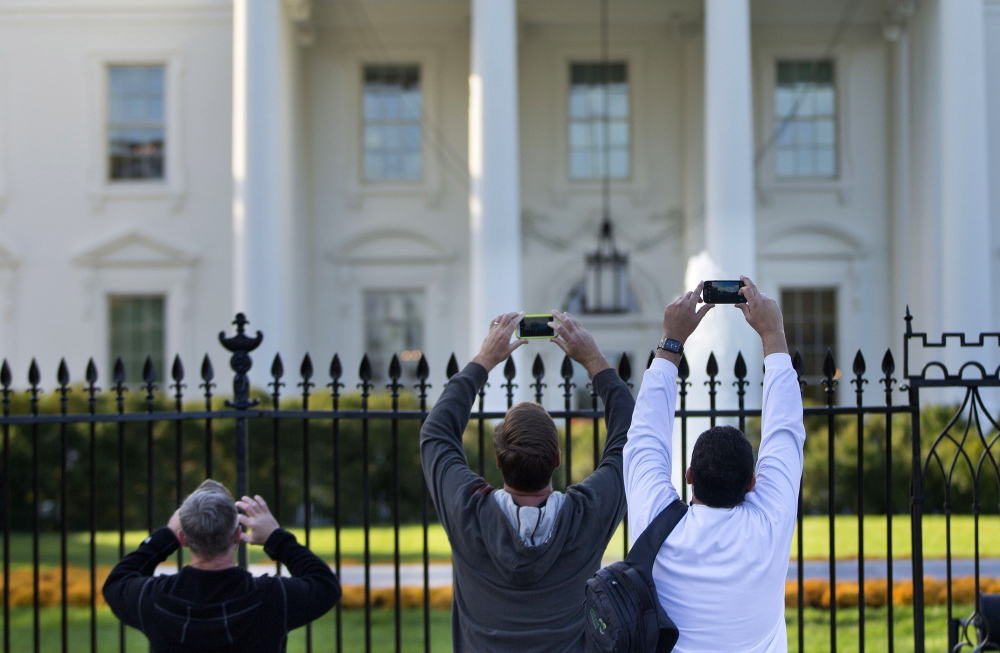 Visitors take photos from the sidewalk in front of the White House. The Secret Service is adding more spikes to the White House fence.