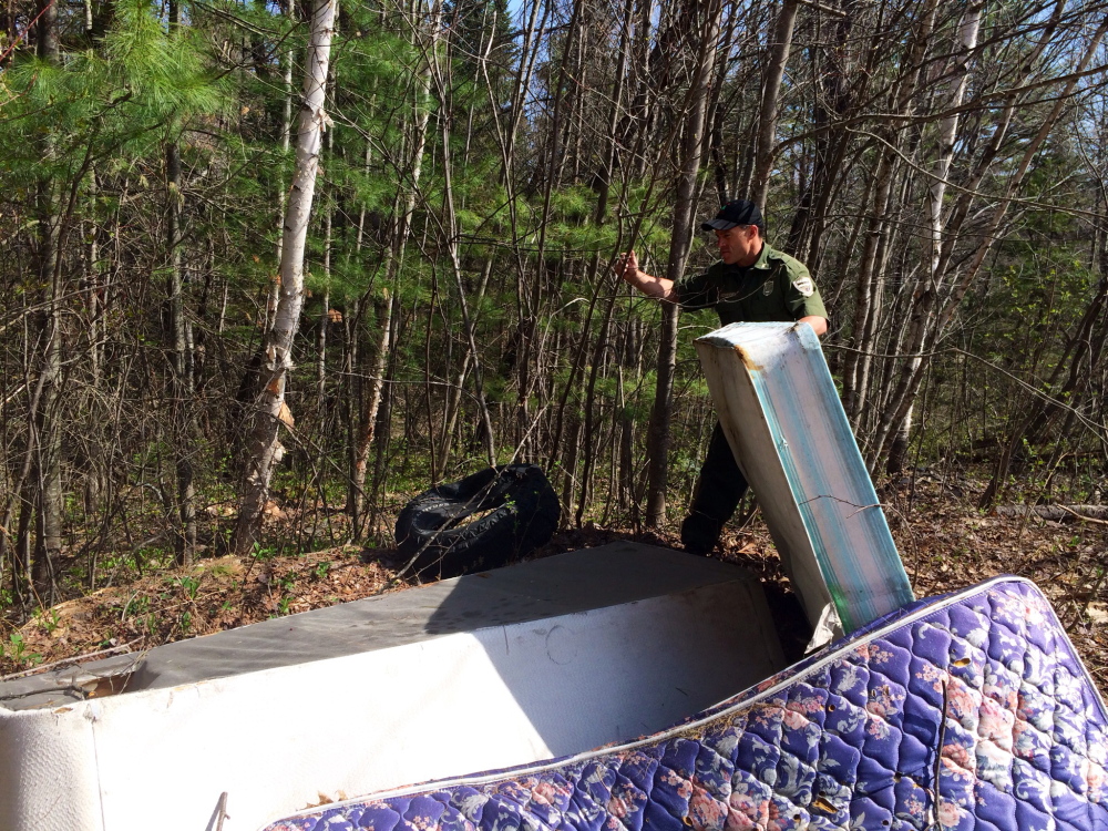 Game Warden Tom McKenny sorts through a pile of mattresses illegally dumped on private property off Martin Stream Road in Fairfield. Reports of illegal dumping have grown from just 2 to 3 percent of all complaints to forest rangers about 20 years ago to 13 percent of all calls in 2013.