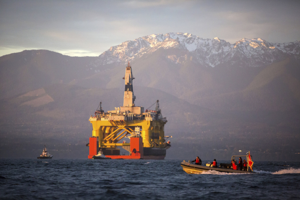 Against the backdrop of the Olympic Mountains, a small boat crosses in front of an oil drilling rig as it arrives in Port Angeles, Wash., aboard a transport ship after traveling across the Pacific. 