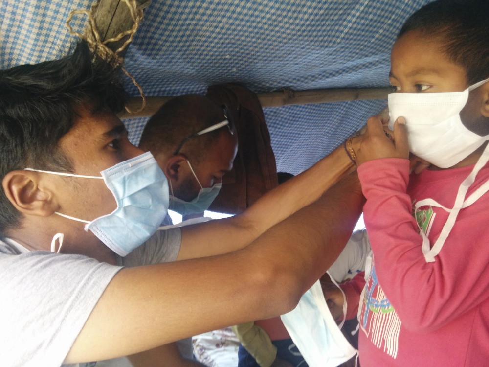 Surya Karki, left, a native of Nepal and a student at College of the Atlantic in Bar Harbor, assists a Nepalese child in securing a face mask in the village of Taudaha.