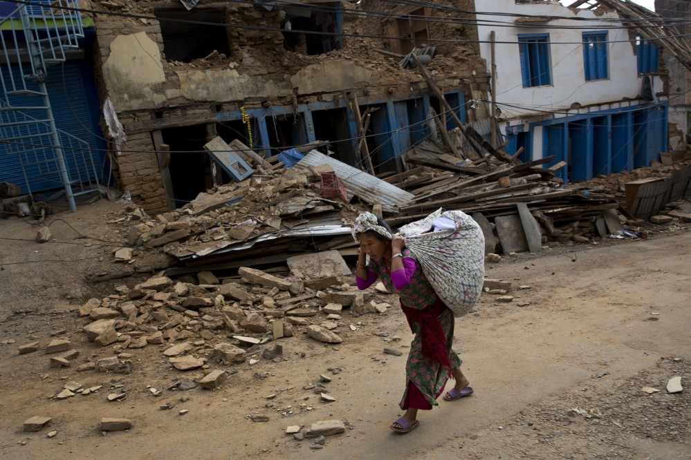 A Nepalese woman carrying belongings walks past a damaged house in Chautara, Nepal, Wednesday.