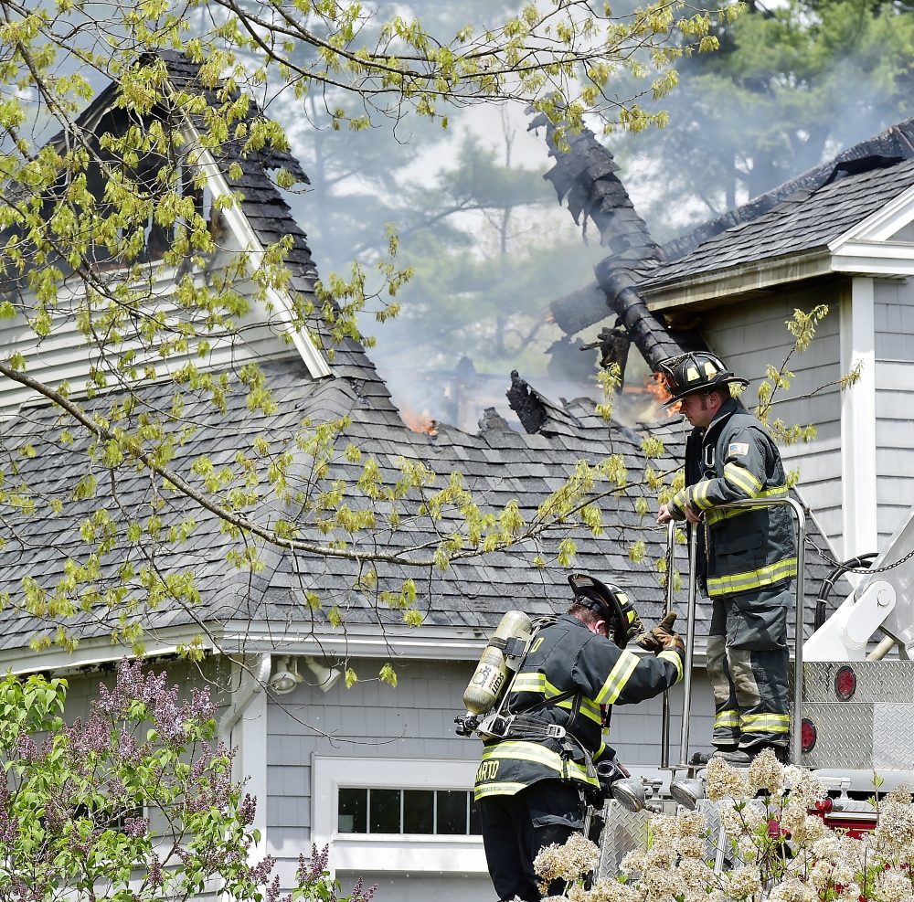 Firefighters climb down from a ladder truck while fighting a house fire at 2 Beaver Brook Road in Scarborough on Friday.