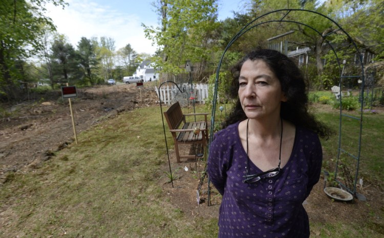 Julie Claffey stands near the memorial gardens where she buried her husband’s ashes at her Scarborough home. When she tried to block her neighbors from putting in a driveway on their property at left, the town did a review, then stopped interceding for her.