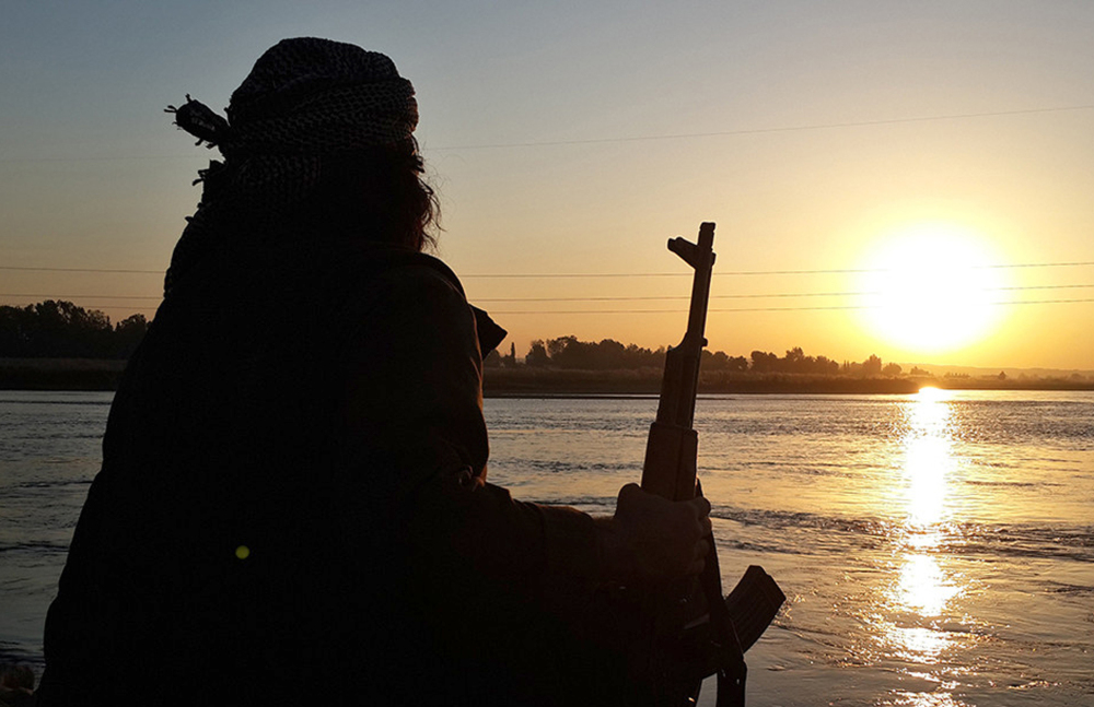 In a photo released by a militant website, an Islamic State jihadi holds an AK-47 as he relaxes by the banks of the Euphrates River in Raqqa, Syria.