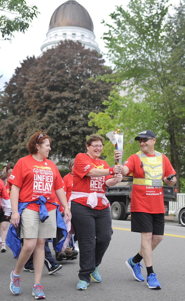 Sarah Porter, center, carries a torch past the State House in Augusta on the first leg of the Special Olympics Unified Relay Across America Torch Run. The flame is making its way to Los Angeles for the start of the World Summer Games.