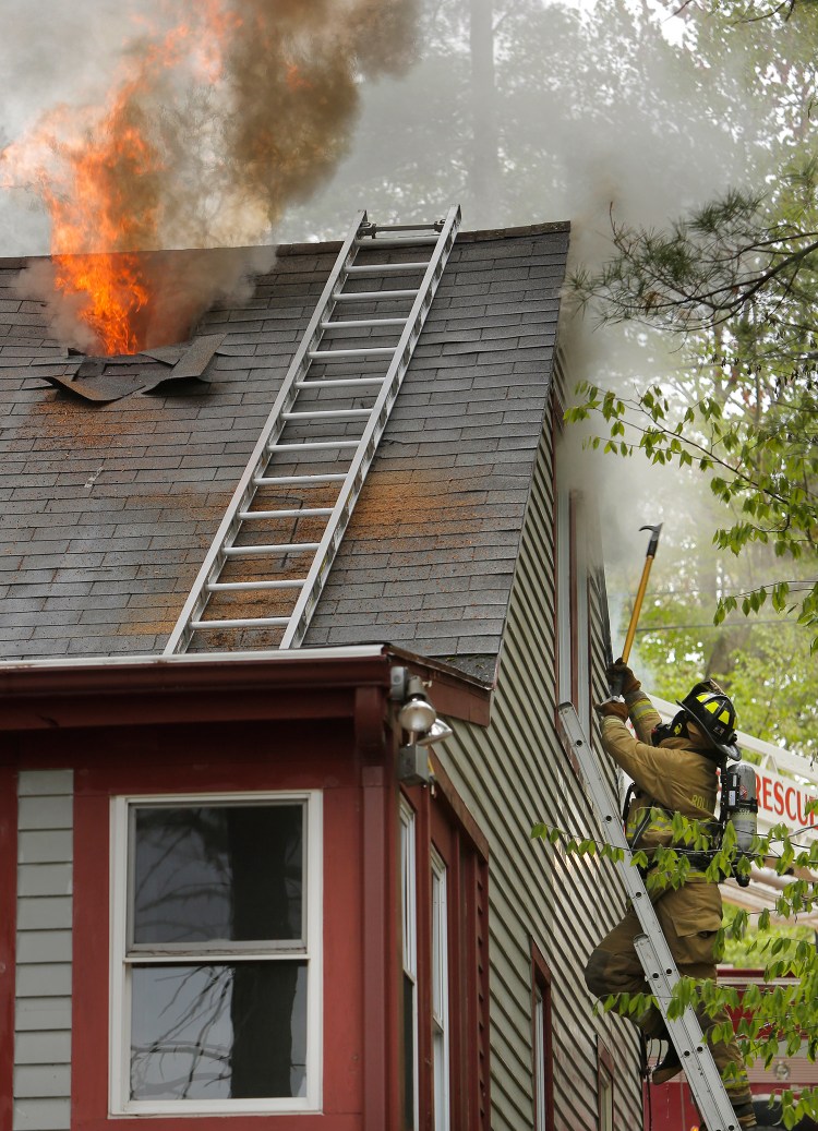 A firefighter breaks through a window while fire vents out the roof of a home on Bauneg Beg Pond in North Berwick on Tuesday. Officials said no one was at home at the time of the fire. 
Gregory Rec/Staff Photographer
