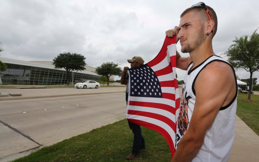 Conner McCasland, right, and Joseph Offutt hold a U.S. flag Tuesday across the street from the Curtis Culwell Center in Garland, Texas, where two suspects were killed Sunday. The Islamic State claimed responsibility for the attack.
