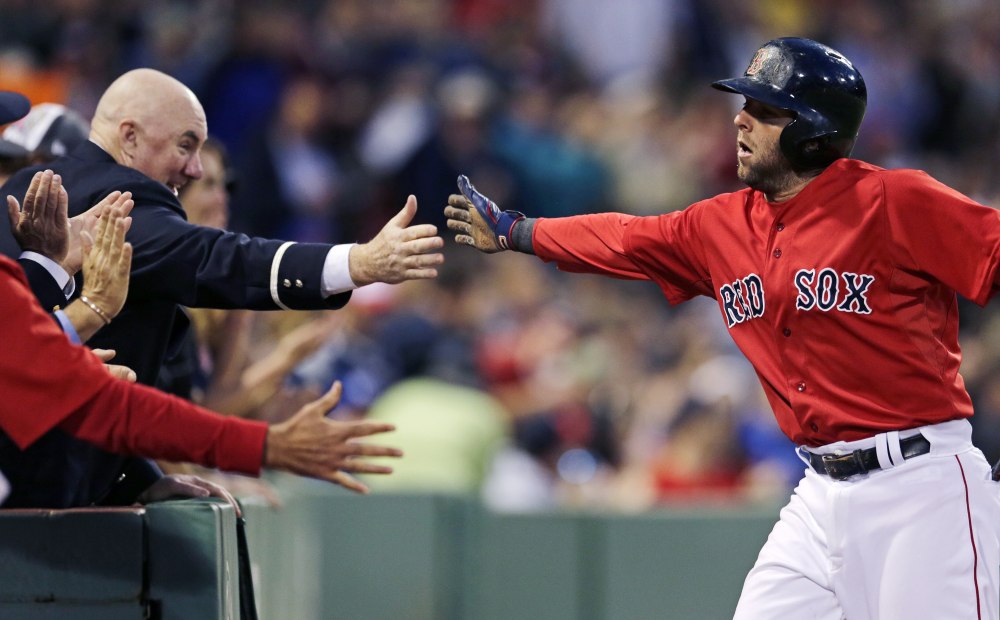 Boston’s Dustin Pedroia is congratulated by fans after scoring on a single by Brock Holt in the fifth inning Friday night against the Oakland Athletics. Pedroia had three hits in the game.