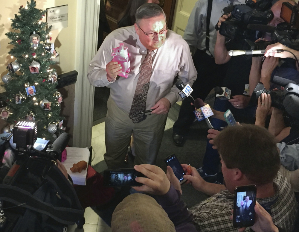 Gov. Paul LePage uses a pink rubber pig and a Christmas tree decorated with pictures of legislative leaders as props to express his disgust with the $6.7 billion budget passed by the Legislature earlier Wednesday.