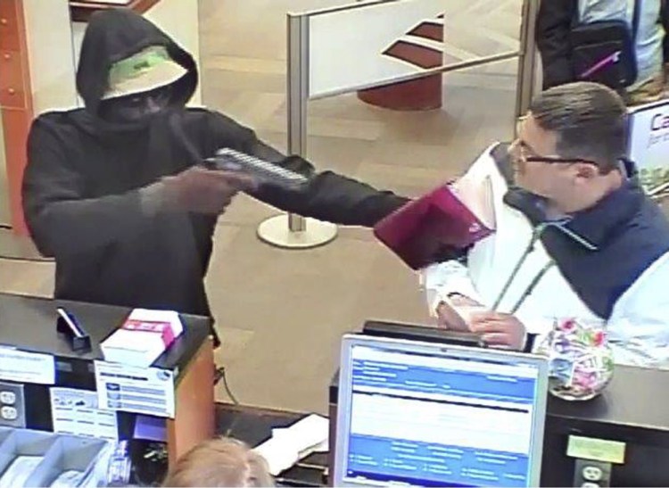 A robber points a gun at a man during the robbery of the Bank of America branch at One City Center in Portland on June 19, in this image from a bank security camera.