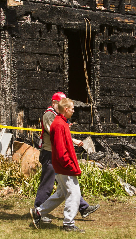 Jonathan Cressey, a resident of the charred house at 305 Cat Mousam Rd. in Kennebunk, walks past the structure with a Red Cross volunteer Monday. Authorities say Cressey climbed from a second-story window and saved his father on the first floor, but couldn’t get to his brother, who died in the blaze early Monday morning.