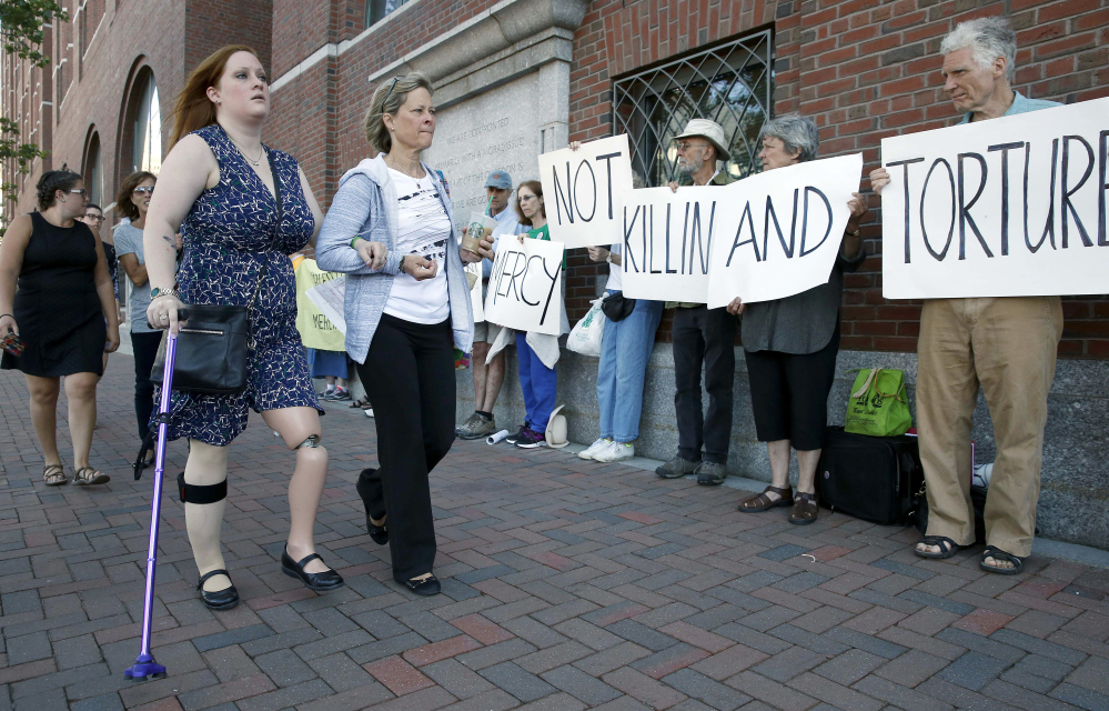 Boston Marathon bombing victim Erika Brannock, foreground left, and her mother Carol Downing, foreground right, walk past demonstrators outside federal court in Boston, on Wednesday. In court, 24 victims and family members of victims spoke of the impact that the Boston Marathon bombing has had on their lives.