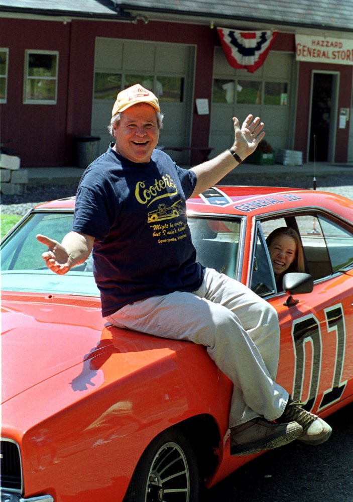 In this Aug. 10, 1999, file photo, “Cooter,” actor Ben Jones, sits atop one of the 229 hotrods, named the General Lee, used in the show “Dukes of Hazzard” as ecstatic fan, Aliceson Johnson, of Charlottesville, Va., sits in the drivers seat in front of his store in Sperryville, Va.