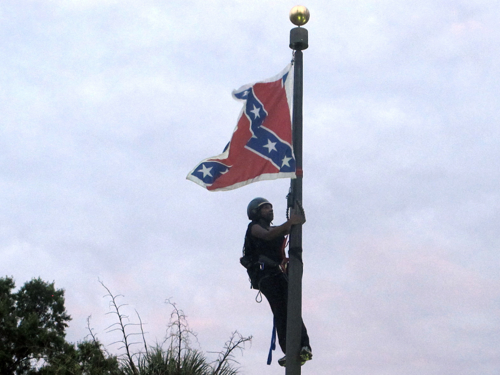 Bree Newsome of Charlotte, N.C., climbs a flagpole to remove the Confederate battle flag at a Confederate monument in front of the Statehouse in Columbia, S.C., on Saturday. She was taken into custody when she came down. The flag was raised again by capitol workers about 45 minutes later.  (AP Photo/Bruce Smith)