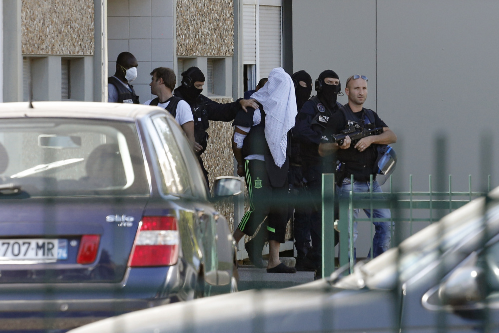 The suspect in the beheading of a businessman, Yassine Salhi, a towel over his head to mask his face, is escorted by police officers as they leave his home in Saint-Priest, outside the city of Lyon, central France, on Sunday.