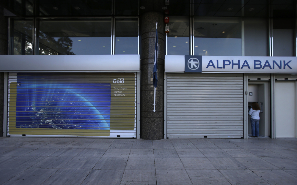 A woman uses an ATM of a closed bank in Athens on Monday. Greece’s five-year financial crisis took its most dramatic turn yet, with the Cabinet deciding that Greek banks would remain shut for six business days and restrictions would be imposed on cash withdrawals.