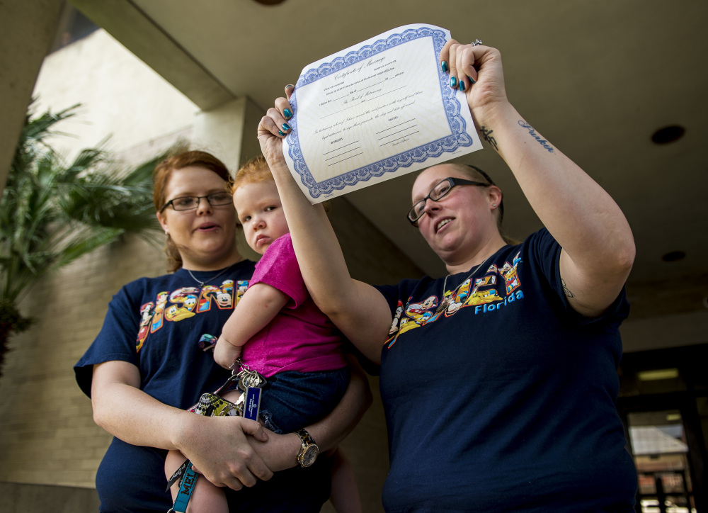 Chelsea Hughes, right, shows her marriage license which she and her partner, Melissa Beckham, left, received at the Lafayette Parish Courthouse in Lafayette, Louisiana, on Monday.
