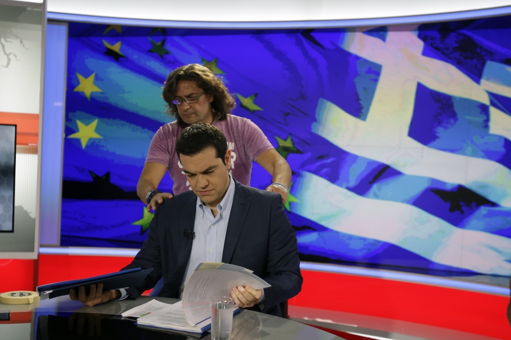 Greek Prime Minister Alexis Tsipras looks at his notes as a technician prepares him for a TV interview. He urges voters to reject creditors’ demands in an upcoming referendum.