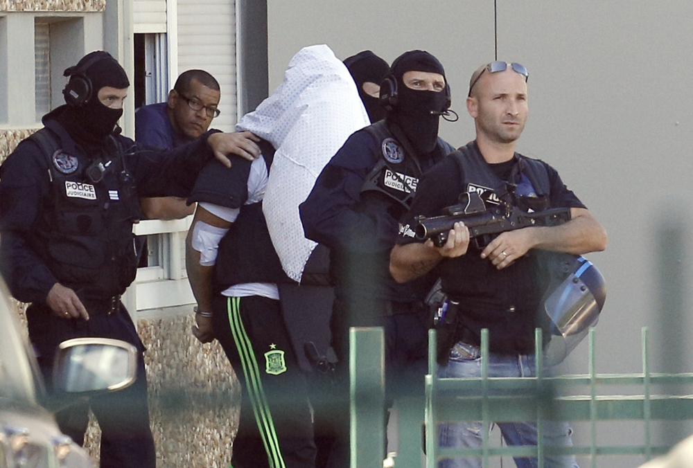 The suspect in the beheading of a businessman, Yassine Salhi, a towel over his head to mask his face, is escorted by police officers as they leave his home in Saint-Priest, outside the city of Lyon, central France, Sunday.
