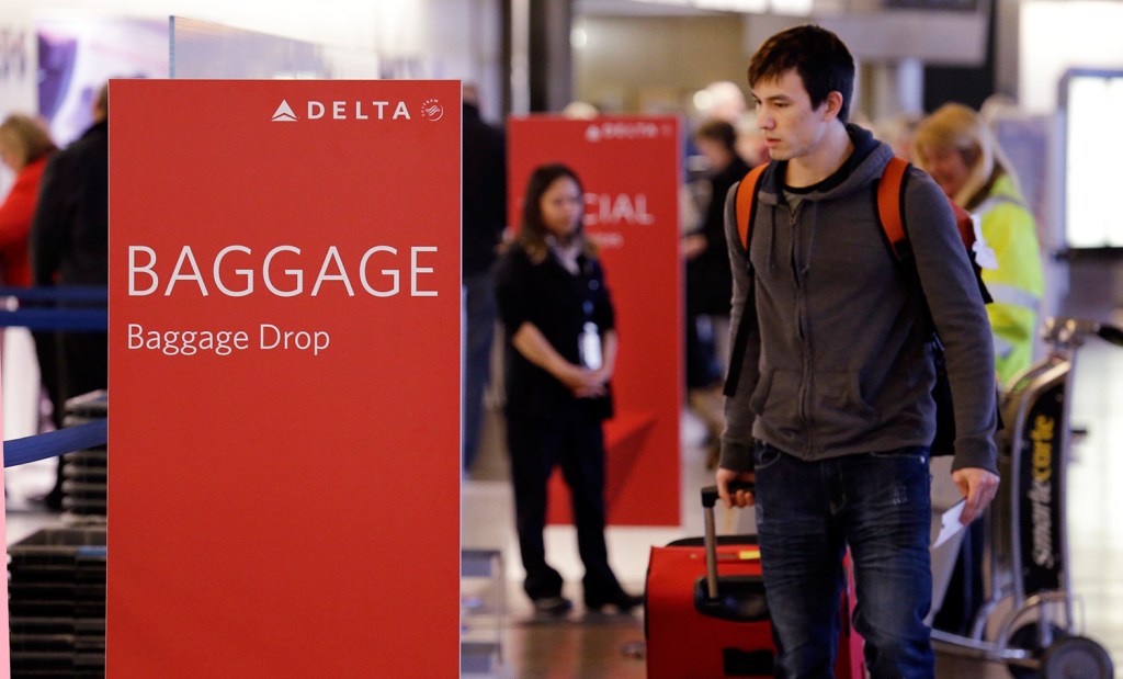Travelers walk toward the baggage drop area for Delta airlines at Seattle-Tacoma International Airport in March. This summer travel season, Delta plans to preload carry-on bags above passengers’ seats on some flights. 
The Associated Press